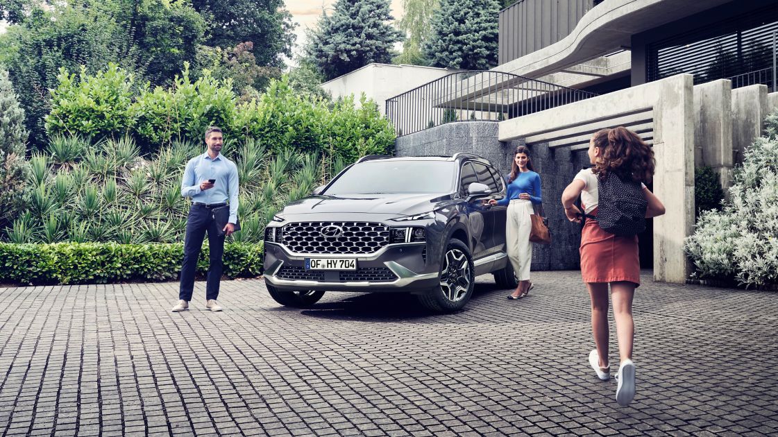 The new Hyundai SANTA FE Hybrid 7 seat SUV in grey parked in front of a luxurious family house.